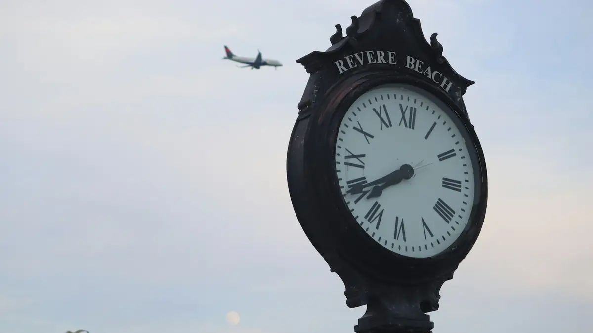 The Revere Beach street clock against a pale sky, a plane passing overhead - Leak Detection in Revere